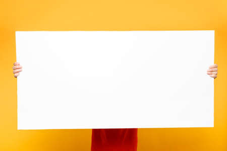 Delivery man in red uniform isolated on yellow orange background. Male employee courier in cap, t-shirt holding big white empty blank billboard with copy space, place for text image. Service conceptの写真素材