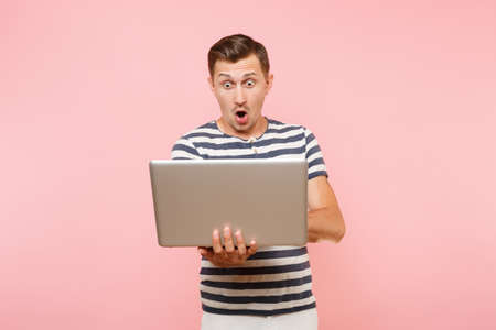 Portrait of sad upset young man wearing striped t-shirt working on laptop computer, copy space...