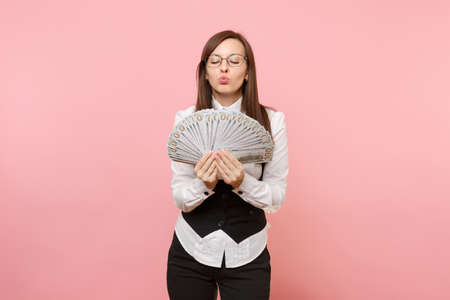 Young business woman in glasses holding bundle lots of dollars, cash money blowing lips kissing isolated on pink background. Lady boss. Achievement career wealth concept. Copy space for advertisementの写真素材