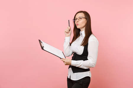 Young puzzled beautiful business woman in glasses holding clipboard tablet with papers document isolated on pink background. Lady boss. Achievement career wealth concept. Copy space for advertisementの写真素材