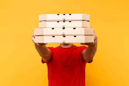 Delivery man in red cap, t-shirt giving food order pizza boxes isolated on yellow background. Male employee pizzaman or courier in uniform holding italian pizza in cardboard flatbox. Service conceptの写真素材