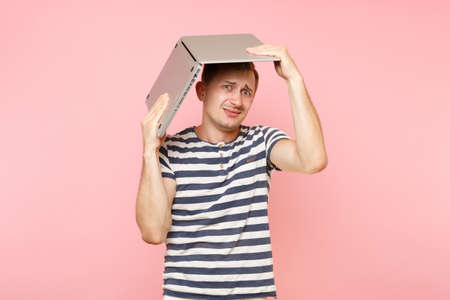 Portrait of handsome young man in striped t-shirt hold above head laptop computer, copy space...