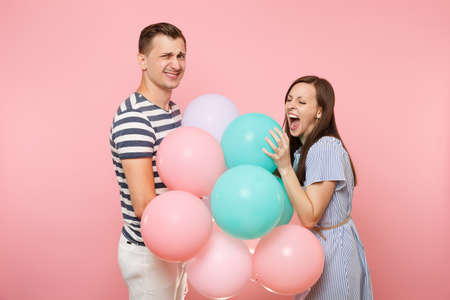 Portrait of young happy smiling couple in love. Woman and man in blue clothes celebrating birthday holiday party on pastel pink background with colorful air balloons. People sincere emotions conceptの写真素材
