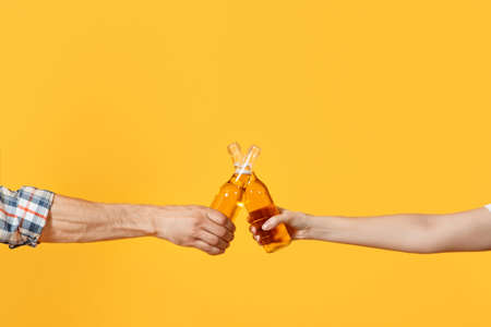Close up cropped of woman and man two hands horizontal holding lager beer glass bottles and clinking...