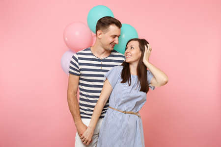 Portrait of young happy smiling couple in love. Woman and man in blue clothes celebrating birthday holiday party on pastel pink background with colorful air balloons. People sincere emotions conceptの写真素材