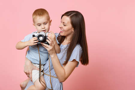 Portrait of happy family. Mother keep in arms, have fun, hug son baby boy, take picture on retro vintage photo camera on pink background. Sincere emotions, Mother's Day, parenthood, childhood conceptの写真素材