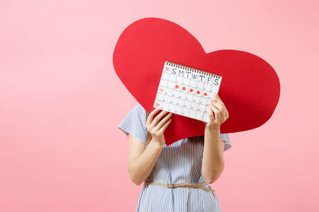 Happy woman in blue dress summer hat holding empty blank red heart, female periods calendar, checking menstruation days isolated on background. Medical healthcare gynecological concept. Copy spaceの写真素材