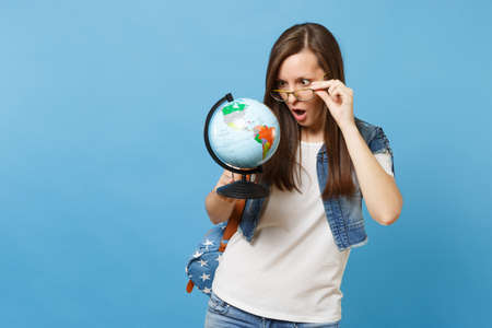 Portrait of young shocked concerned woman student with opened mouth with backpack removing glasses...