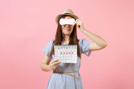 Woman in blue dress, hat holding sanitary napkin, cover eyes, female periods calendar for checking menstruation days isolated on pink background. Medical healthcare, gynecological concept. Copy spaceの写真素材