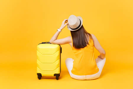 Traveler tourist woman in summer casual clothes, hat sit with suitcase isolated on yellow orange background. Female passenger traveling abroad to travel on weekends getaway. Air journey conceptの写真素材