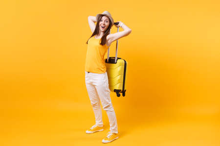 Traveler tourist woman in summer casual clothes, hat with suitcase isolated on yellow orange background. Female passenger traveling abroad to travel on weekends getaway. Air flight journey conceptの写真素材