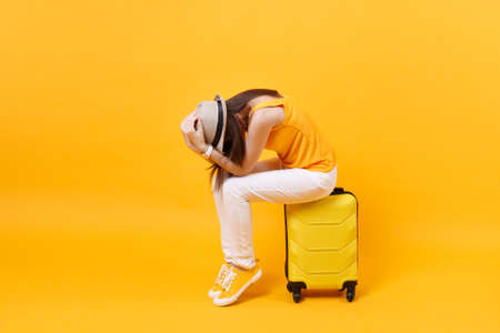 Upset tourist woman in summer casual clothes sit on suitcase put hands on head isolated on yellow orange background. Female traveling abroad to travel on weekends getaway. Air flight journey conceptの写真素材