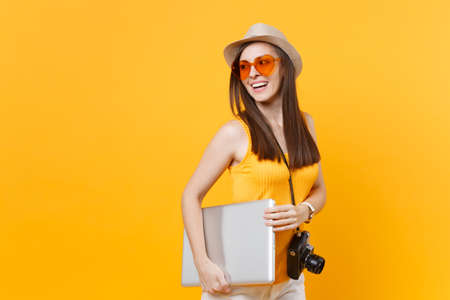 Traveler tourist woman in summer casual clothes, hat keeping laptop pc computer underarm isolated on yellow orange background. Female traveling abroad travel on weekends getaway. Air journey conceptの写真素材