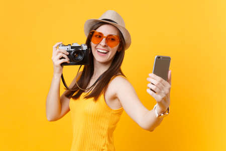 Tourist woman in summer casual clothes, hat doing taking selfie shot on mobile phone isolated on yellow background. Female passenger traveling abroad to travel on weekends getaway. Air flight conceptの写真素材