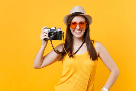 Tourist woman in summer casual clothes, hat take picture on retro vintage photo camera isolated on yellow background. Girl traveling abroad to travel on weekends getaway. Air flight journey conceptの写真素材