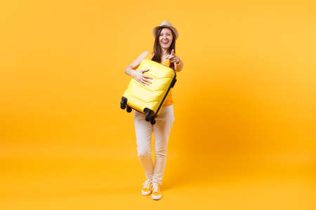 Traveler tourist woman in summer casual clothes, hat with suitcase isolated on yellow orange background. Female passenger traveling abroad to travel on weekends getaway. Air flight journey conceptの写真素材