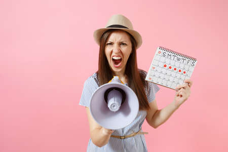 Angry expression wild woman screaming in megaphone, holding periods calendar for checking menstruation days isolated on pink background. Medical healthcare, pms mood gynecological concept. Copy spaceの写真素材