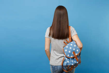 Back rear view of young brunette woman student in casual clothes with backpack standing isolated on blue background. Education in high school university college. Copy space for advertisementの写真素材