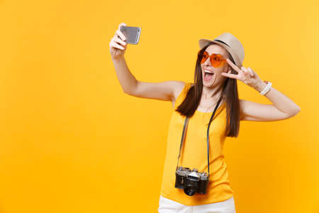Tourist woman in summer casual clothes, hat doing taking selfie shot on mobile phone isolated on yellow background. Female passenger traveling abroad to travel on weekends getaway. Air flight conceptの写真素材