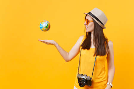 Traveler tourist woman in summer casual clothes, hat toss up globe isolated on yellow orange background. Female passenger traveling abroad to travel on weekends getaway. Air flight journey conceptの写真素材