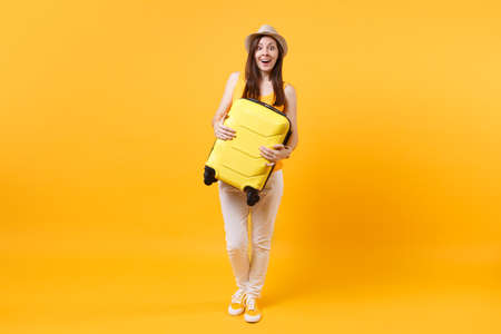 Traveler tourist woman in summer casual clothes, hat with suitcase isolated on yellow orange background. Female passenger traveling abroad to travel on weekends getaway. Air flight journey conceptの写真素材