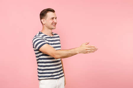 Portrait of smiling young man wearing striped t-shirt standing with outstretched hand for greeting...