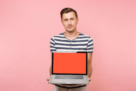 Portrait of young man holding in hand laptop computer with blank black empty screen display copy space isolated on pastel pink background. People sincere emotions lifestyle concept. Advertising areaの写真素材