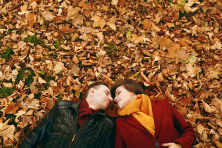Top view Portrait of young romantic couple in love woman and man with closed eyes facing each other lying on fallen leaves in autumn city park outdoors. Love relationship family lifestyle conceptの写真素材