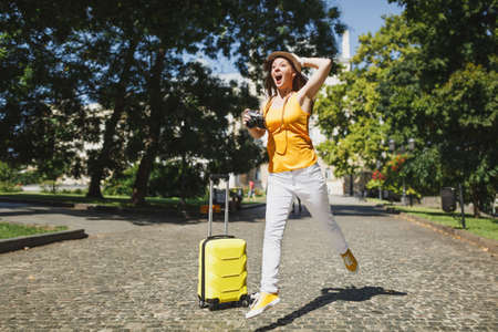 Shocked traveler tourist woman with suitcase screaming clinging to head holding retro vintage photo...