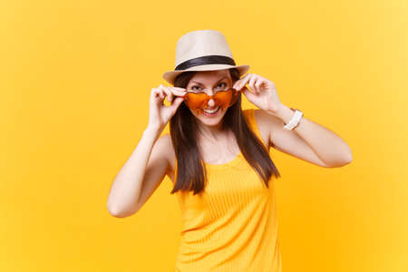 Portrait of excited smiling young woman in straw summer hat, put hands on orange heart glasses, copy space isolated on yellow background. People sincere emotions, lifestyle concept. Advertising areaの写真素材