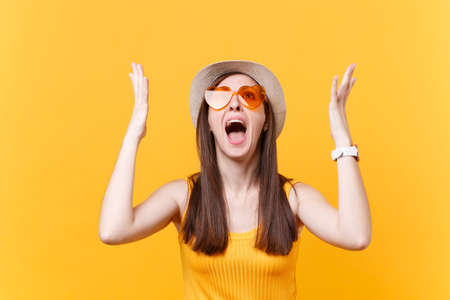Portrait of expressive screaming sad upset woman in orange glasses spreading hands, keeping mouth...