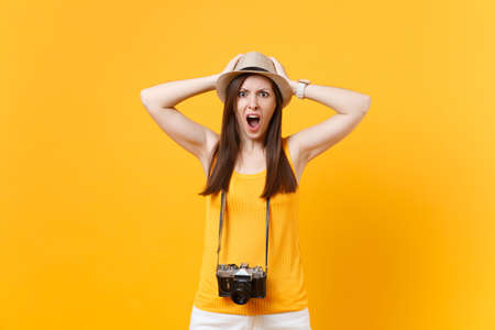 Shocked tourist woman in summer casual clothes, hat with retro vintage photo camera isolated on yellow orange background. Girl traveling abroad travel on weekends getaway. Air flight journey conceptの写真素材