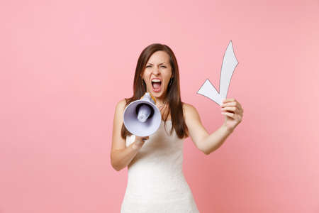 Angry bride woman in wedding dress screaming in megaphone holding check mark isolated on pink pastel background. Wedding to do list. Organization of celebration concept. Copy space for advertisementの写真素材