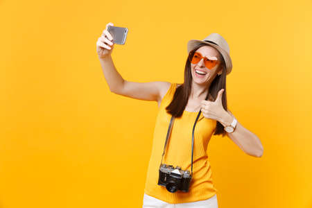 Tourist woman in summer casual clothes, hat doing taking selfie shot on mobile phone isolated on yellow background. Female passenger traveling abroad to travel on weekends getaway. Air flight conceptの写真素材