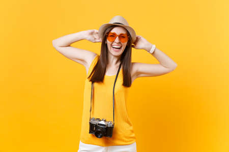 Happy traveler tourist woman in summer casual clothes, hat with retro vintage photo camera isolated on yellow orange background. Girl traveling abroad travel on weekends getaway. Air flight conceptの写真素材