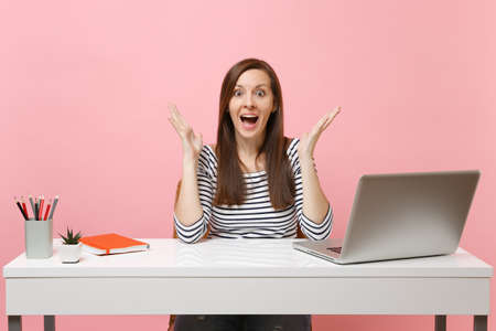 Excited woman in casual clothes spread hands, sit work at white desk with contemporary pc laptop...