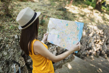 Back view Traveler tourist woman in yellow summer casual clothes, hat looking on city map, search...