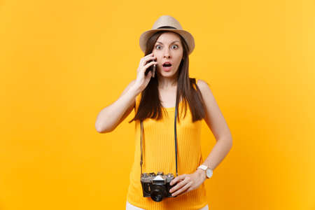 Tourist woman in summer hat talking on mobile phone, calling friend, booking taxi, hotel isolated on yellow background. Female traveling abroad to travel on weekends getaway. Air flight conceptの写真素材