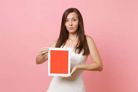 Portrait of pretty bride woman in wedding dress hold tablet pc computer with blank black empty screen isolated on pastel pink background. Wedding to do list. Organization of celebration. Copy spaceの写真素材