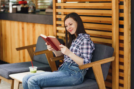 Beautiful woman in outdoors street summer coffee shop wooden cafe sitting in casual clothes, reading...