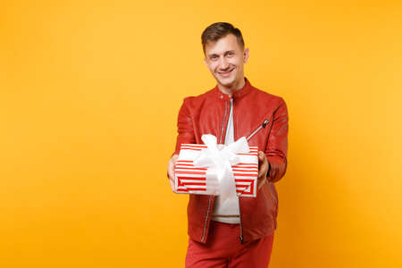 Portrait vogue smiling handsome young man in red jacket, t-shirt hold present box with gift isolated on bright trending yellow background. People sincere emotions lifestyle concept. Advertising areaの写真素材