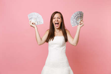Crazy overjoyed bride woman in white wedding dress holding bundle lots of dollars, cash money and...