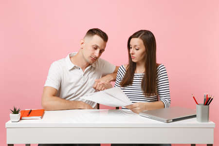 Two young tired business woman man colleagues sit work at white desk with contemporary laptop...