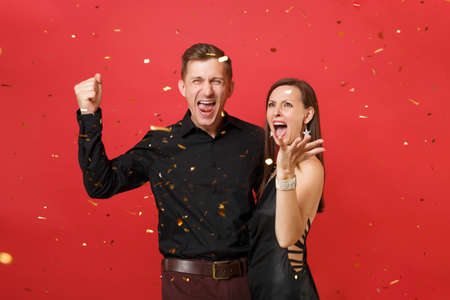 Stunning couple in black clothes celebrating birthday holiday party throw up confetti isolated on bright red background. St. Valentine's International Women's Day Happy New Year 2019 concept. Mock upの写真素材