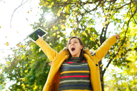 The beautiful happy cheerful brown-haired woman in a yellow coat and striped longsleeve rejoices...