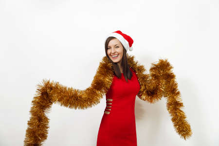 The beautiful caucasian young happy woman with healthy skin and charming smile in red dress, Christmas hat and garland of tinsel on white background. Santa girl isolated. New Year holiday 2018 conceptの写真素材