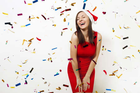 The beautiful caucasian young happy woman wearing red dress and Christmas hat laughing with her eyes closed with pleasure on white background with confetti. Santa girl. New Year holiday 2018 conceptの写真素材
