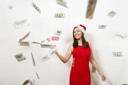 The beautiful caucasian young happy woman in red dress and Christmas hat holding card number 2018...