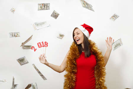 Caucasian young happy woman in red dress, tinsel and Christmas hat holding card number 2018 and...