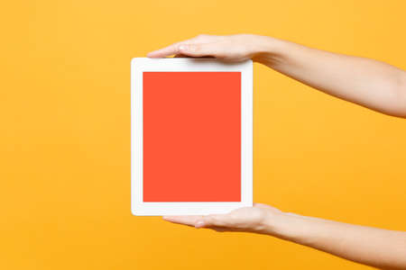 Close up female hold in hand tablet pc pad with blank empty screen with place for text or image, workspace isolated on trending yellow orange background. Technology concept. Copy space advertisementの写真素材